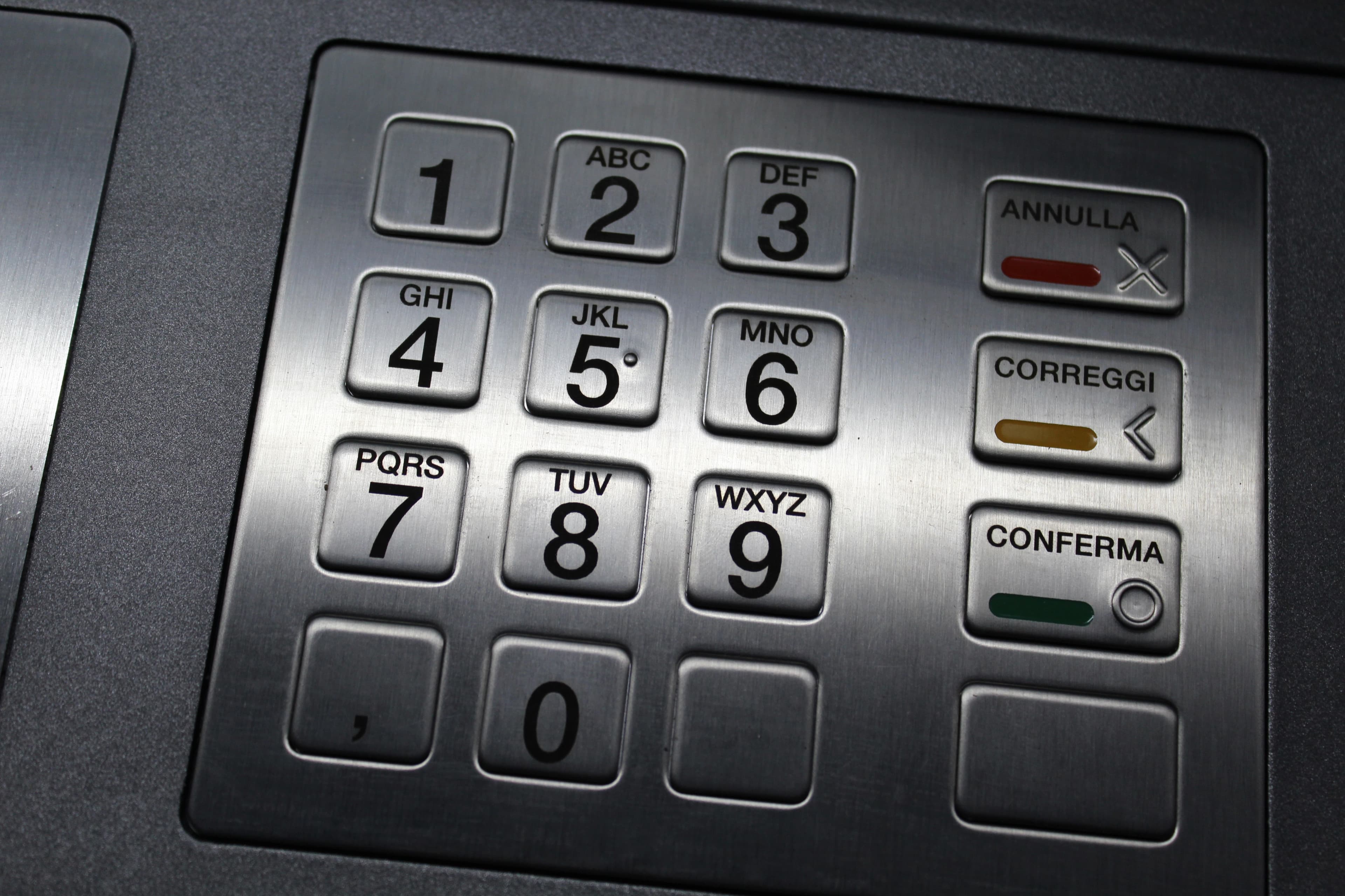 An Italian ATM keypad with keys labelled Annulla, Correggi and Conferma, marked with a red X, a yellow left arrow and a green circle, and a raised dot on the 5