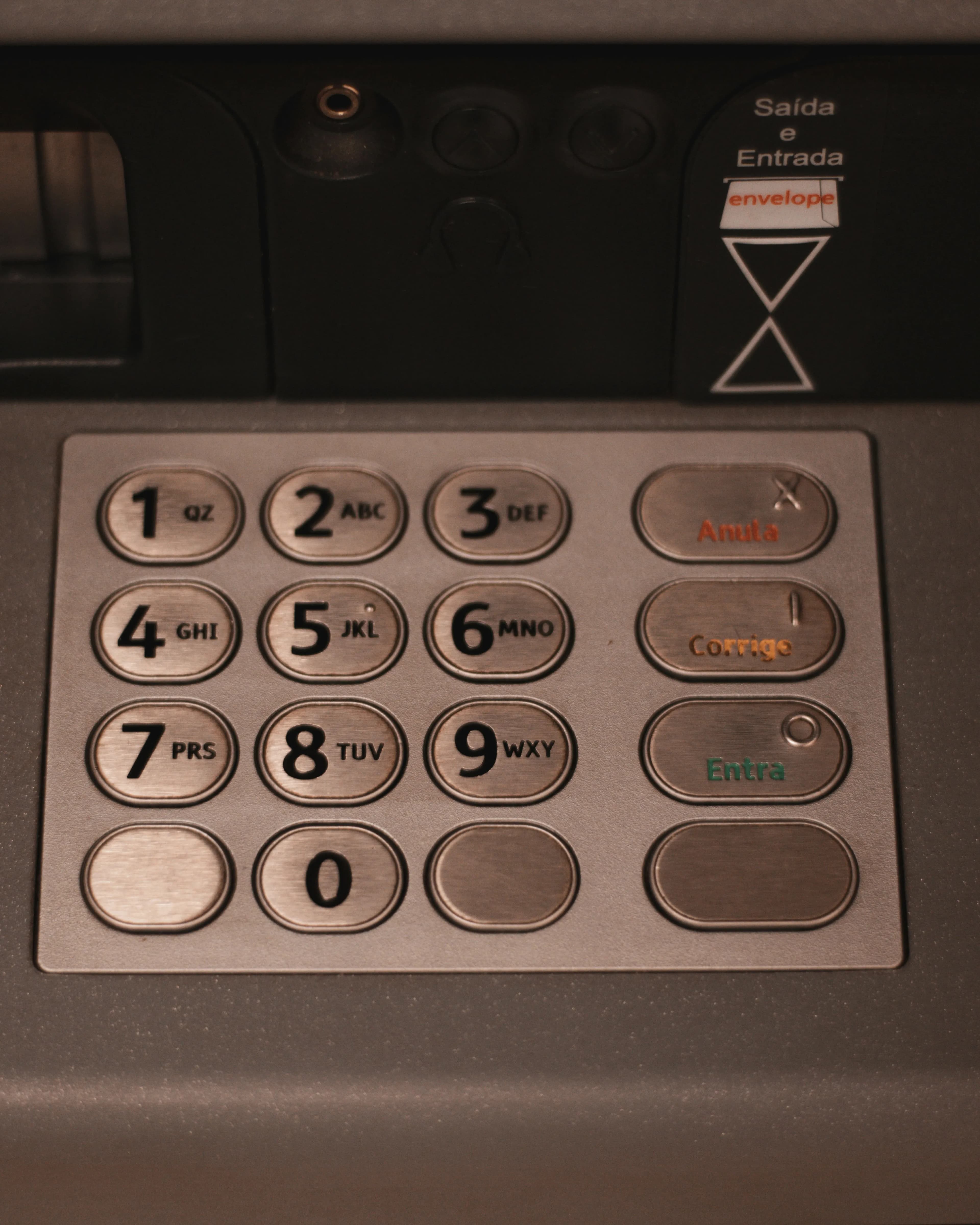 Close-up of a metal ATM keypad with numbered and coloured keys