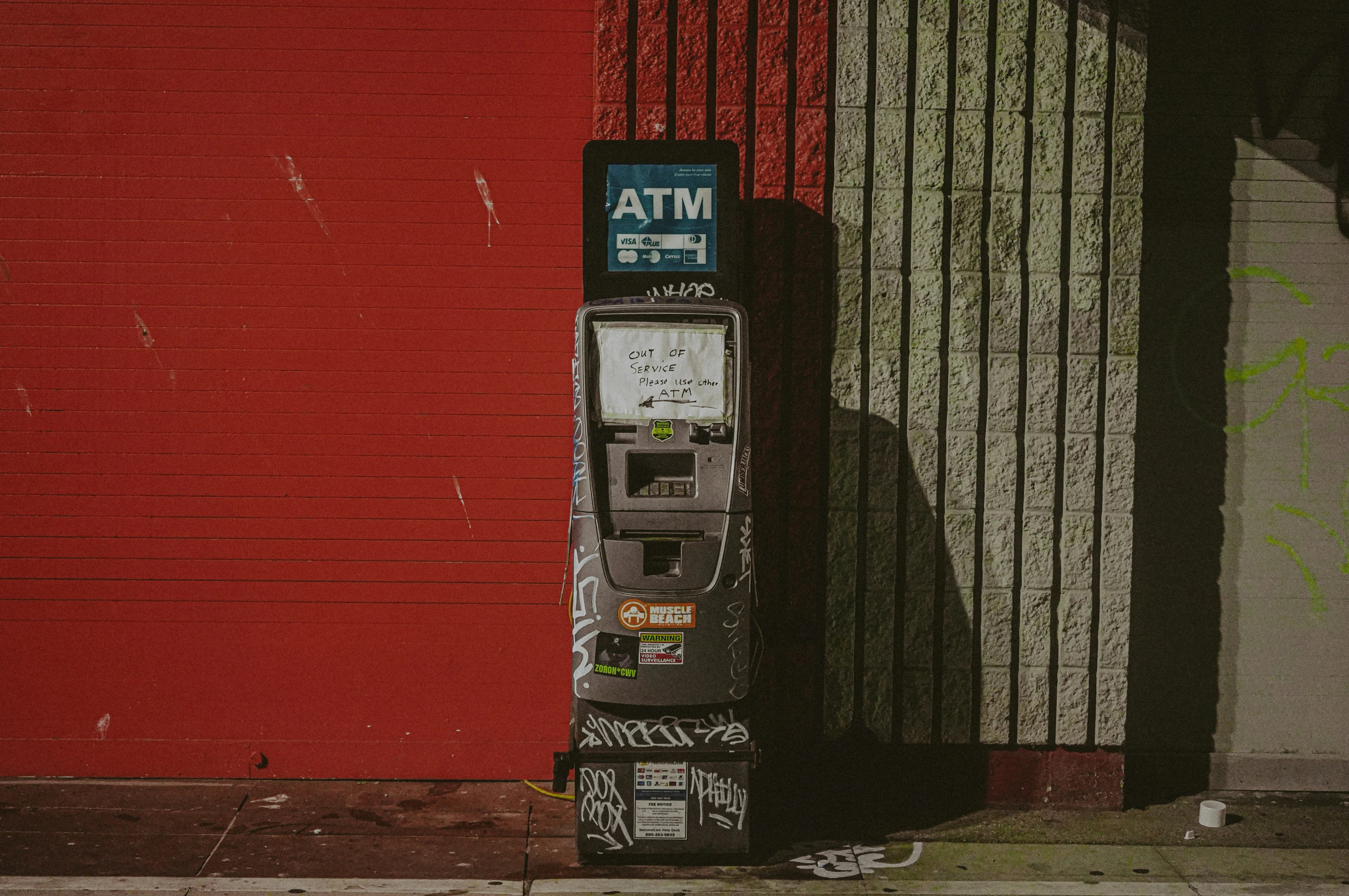 A weathered free-standing ATM against a red wall